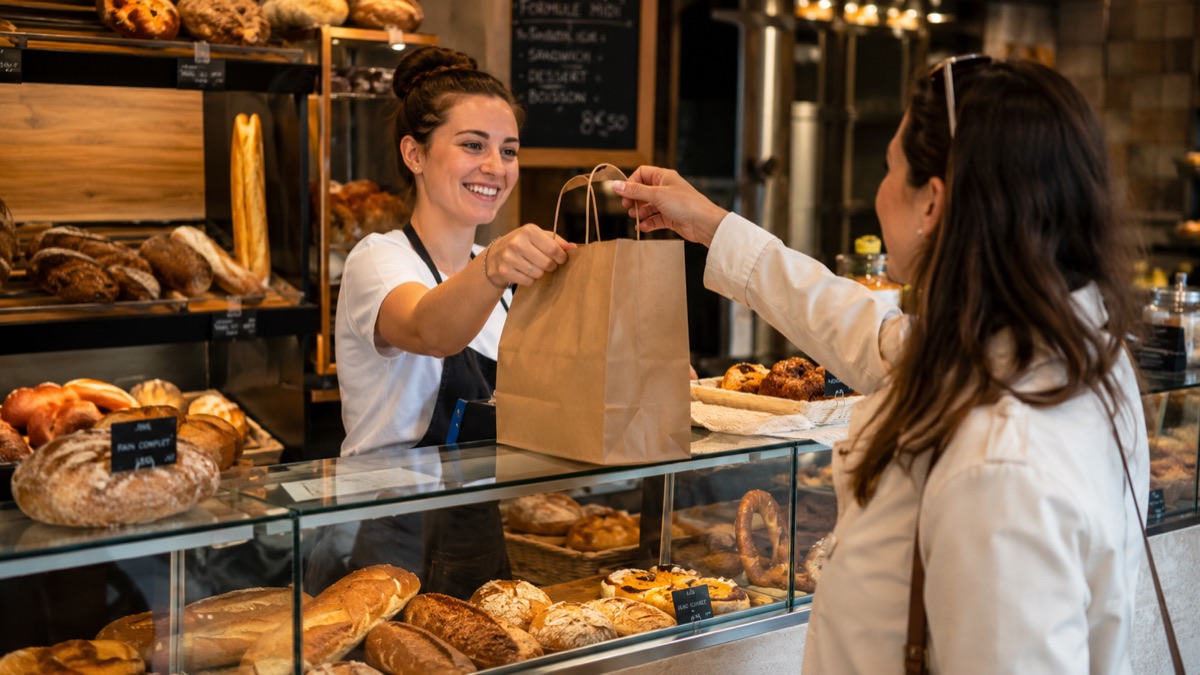 Une boulangère tend un sac en papier à une cliente