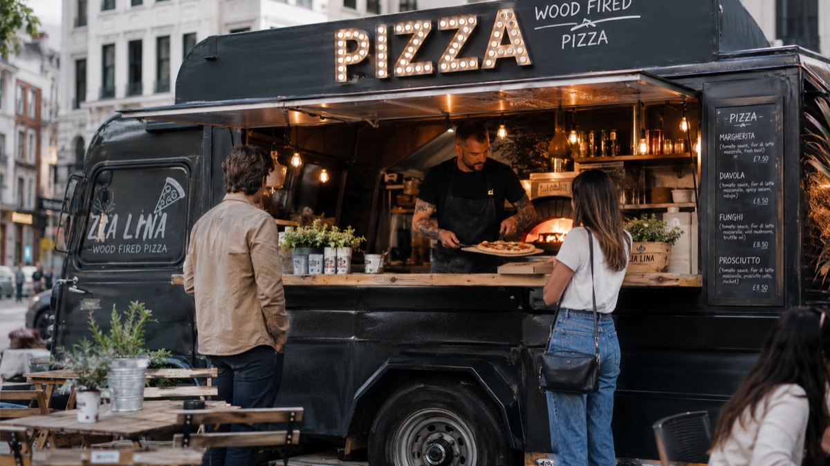 Un pizzaïolo sert une pizza depuis son camion à deux clients
